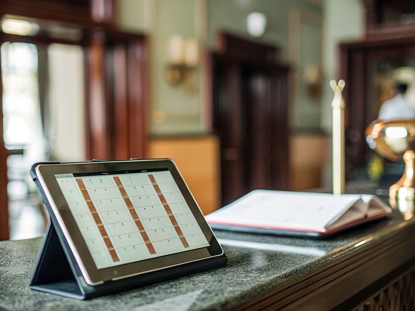 OTA parity and direct booking strategy: tablet showing a booking calendar on a hotel concierge desk