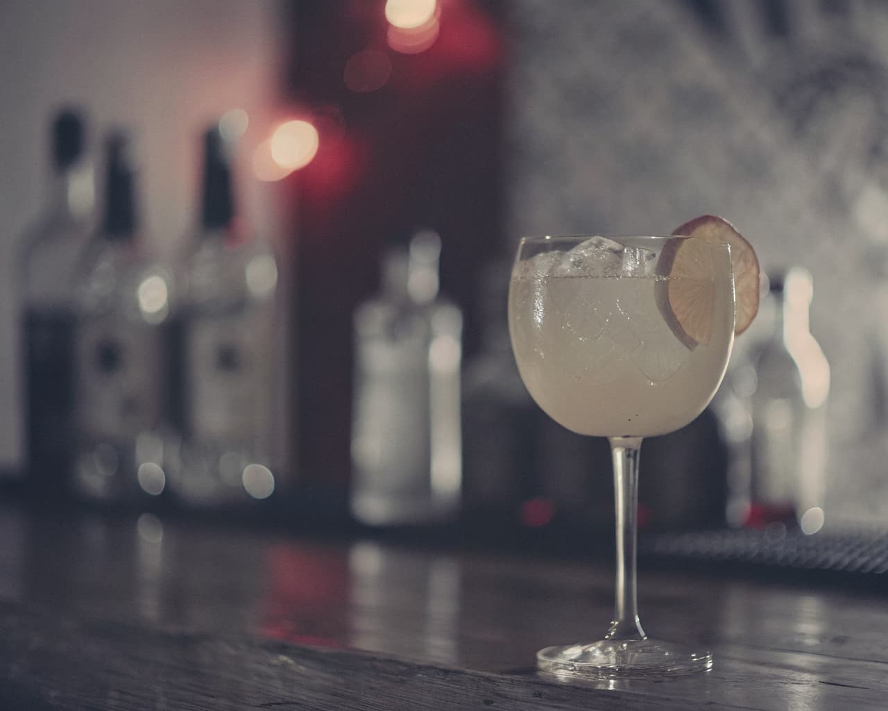 Craft cocktail with citrus garnish on a dark wood bar counter with amber bokeh lighting