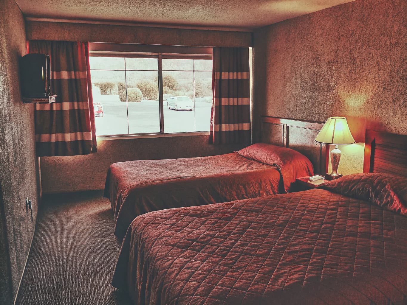 Clean, simple motel room interior with two beds and a parking lot view