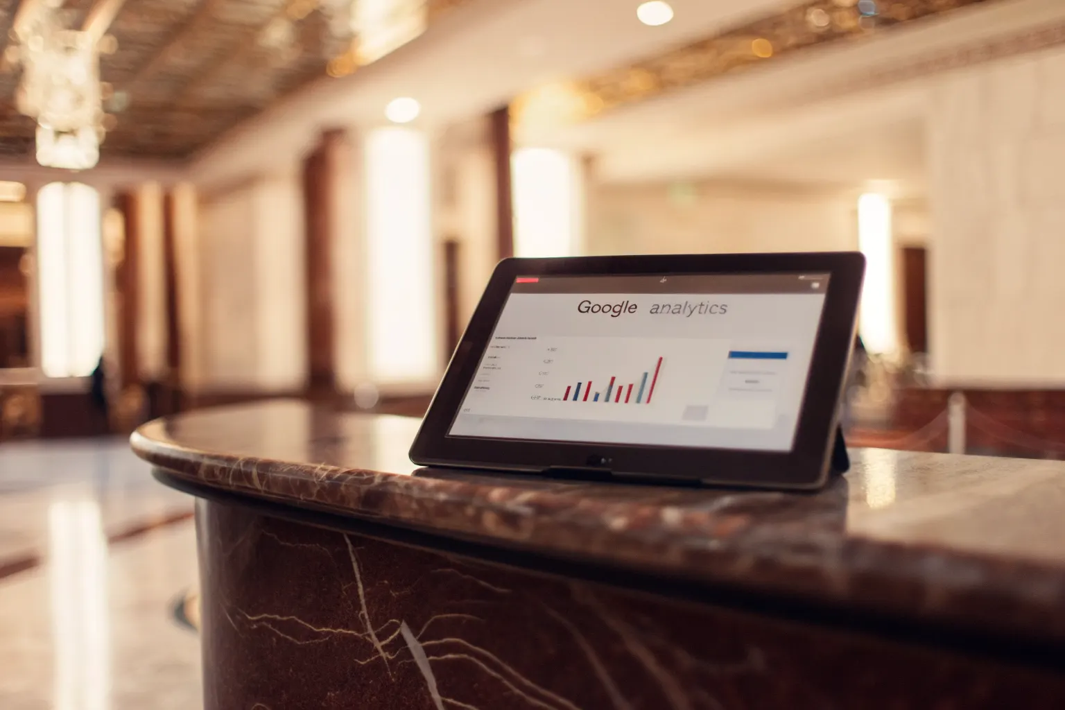 Analytics dashboard on tablet at a hotel concierge desk showing mobile marketing performance metrics and booking trends